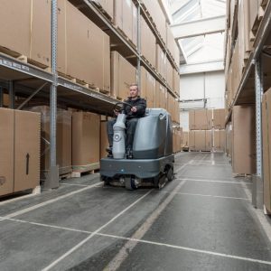 מכונת שטיפה רכובה דגם SC6500 1100 בחלל מחסן עם קירות מלאים בקופסאות קרטון.